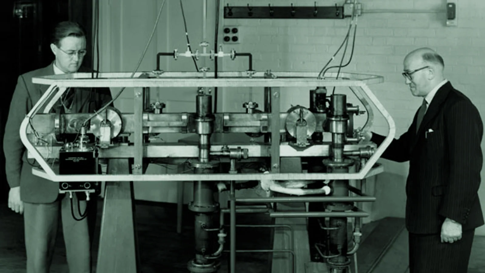 Researchers standing beside an early laboratory atomic clock.